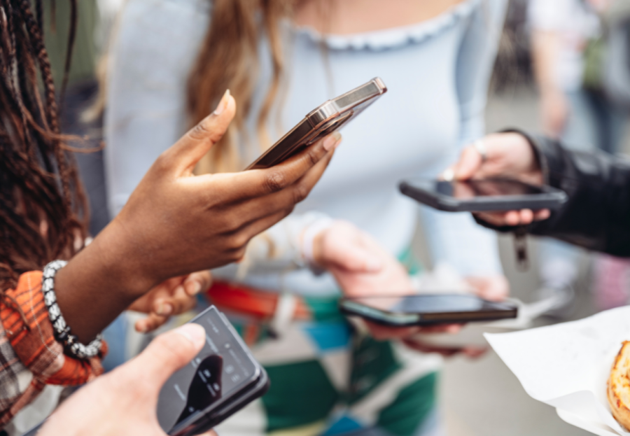 Four people stand in a huddle but the image focuses only on the mobiles they are holding in their hands. One screen shows a thumb hovering over the Follower button on social media, representing the importance of brand awareness ads in building a customer base.