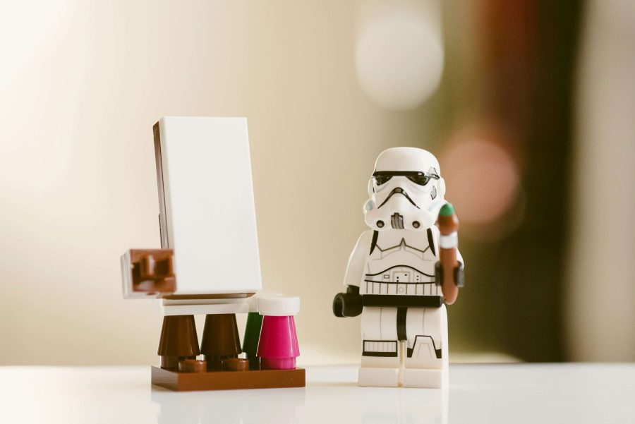 A toy character of stormtrooper stands next to a toy drawing board. They have a paint brush in one hand ready to paint a strategy.