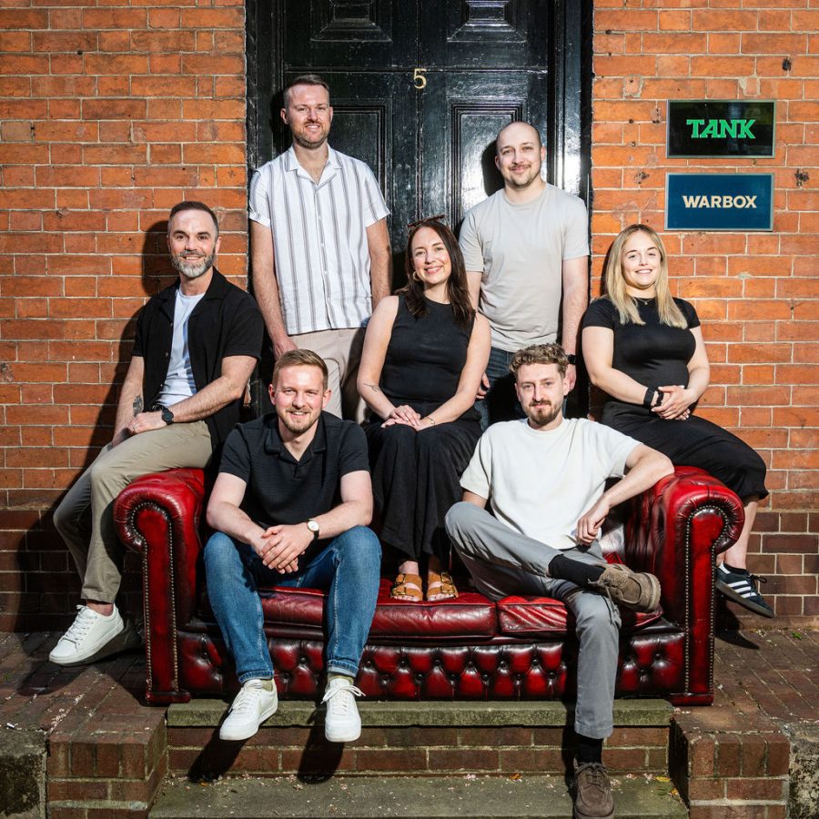 Tank team sit on and around a big red leather sofa and smile at the camera. Happy with PR Week Top 150 results.